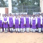 A large group of St. John's S.S - Ikumba students in purple uniforms assembled near the school campus entrance gate.