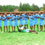St. John's SS Ikumba female netball team standing together in uniform on the school sports field.