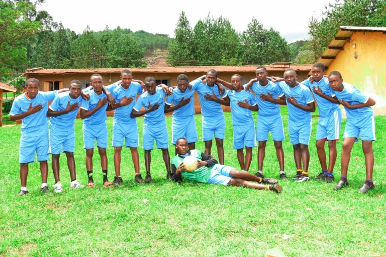 St. John's SS Ikumba female netball team standing together in uniform on the school sports field.