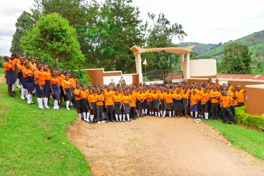 A large gathering of students in matching orange uniforms attending an assembly inside the open pavilion hall at St. John's S.S - Ikumba.